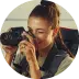 Woman with a ponytail, smiling, holding and looking through the lens of a camera from the side